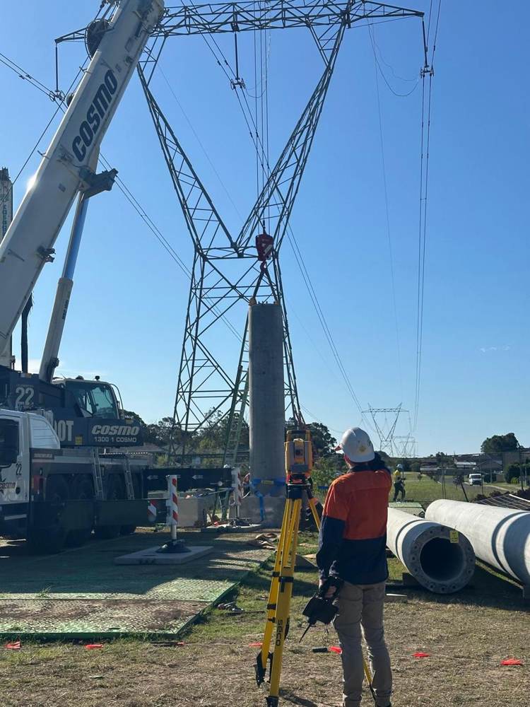 Pole being placed beside a transmission tower